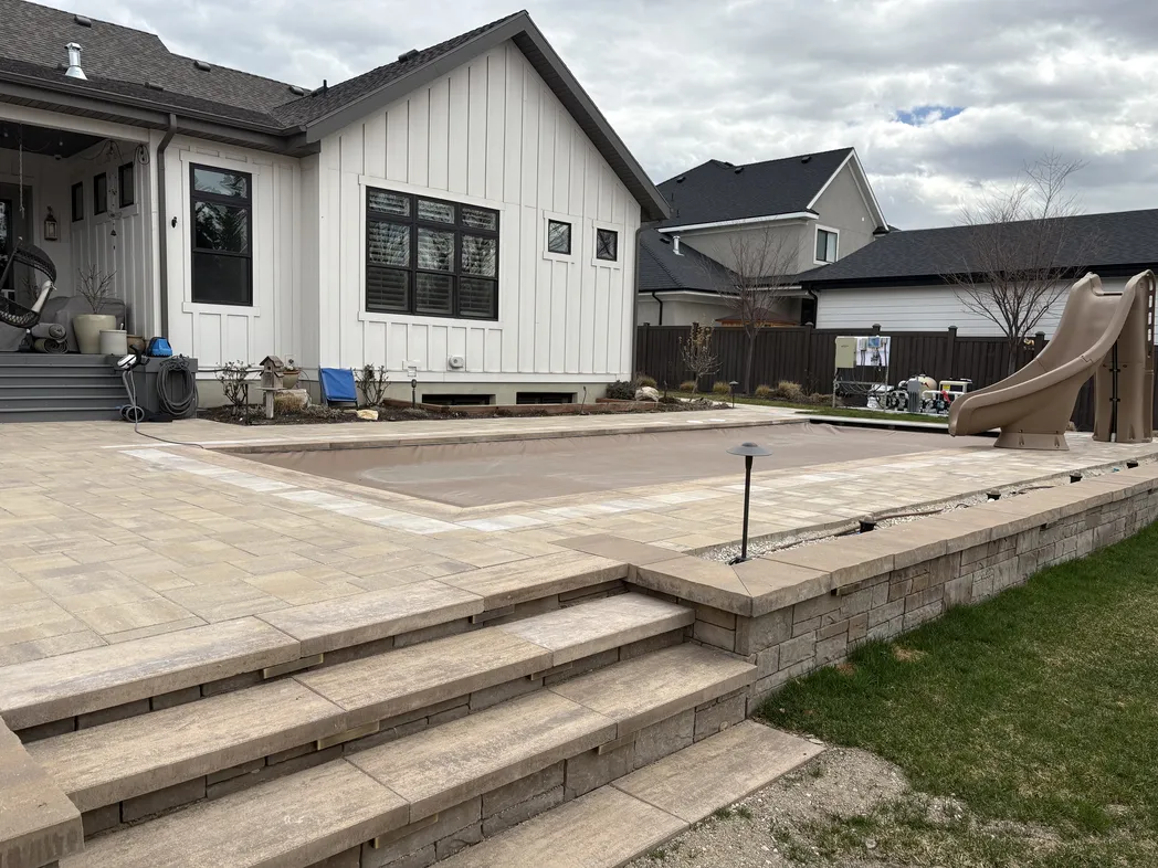 Large custom paver patio with steps beside a residential pool area